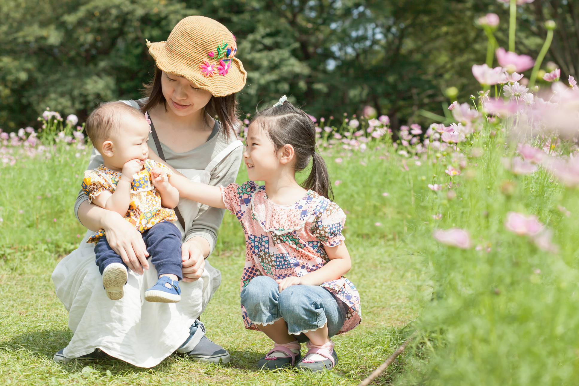 一面に花が咲いた野原で遊ぶ二人の子供とお母さん